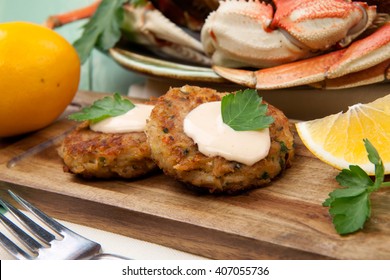 Three Crab Cakes Appetizer With Spicy Sauce And Fresh Parsley. Dungeness Crab In The Background.
