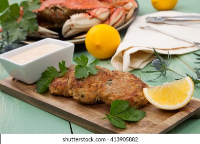 Three Crab Cakes Appetizer With Spicy Sauce And Fresh Parsley. Dungeness Crab In The Background.
