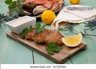 Three Crab Cakes Appetizer With Spicy Sauce And Fresh Parsley. Dungeness Crab In The Background.
