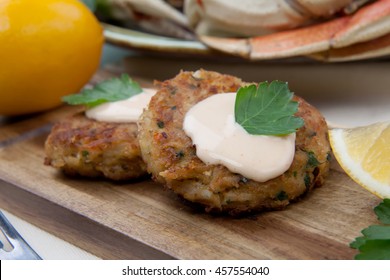 Three Crab Cakes Appetizer With Spicy Sauce And Fresh Parsley. Dungeness Crab In The Background.
