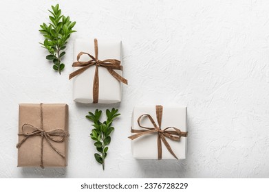 Three craft gift boxes on a white background and green boxwood branches. The concept of holidays and DIY gifts. Postcard, mock-up.