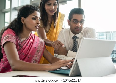 Three creative Indian employees working together around a laptop in a modern office 