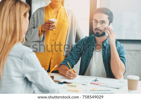 Three creative workers meet together to develop new project, express ideas, drink hot coffee. Young professionals in coworking office use modern technologies, creat business, discuss working questions