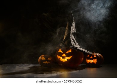 Three creepy Halloween grinning pumpkins glow in the dark among the fog. jack-o-lantern in a witch hat on a black background in smoke. - Powered by Shutterstock