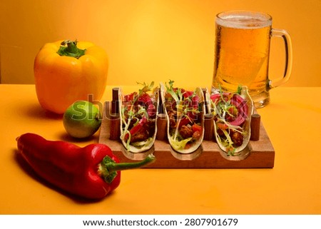 Three crispy chicken tacos served in a wooden taco holder with fresh vegetables, pickled red onions, lime, sweet peppers and colorful ingredients on a vibrant orange background. Mexican street food concept with copy space