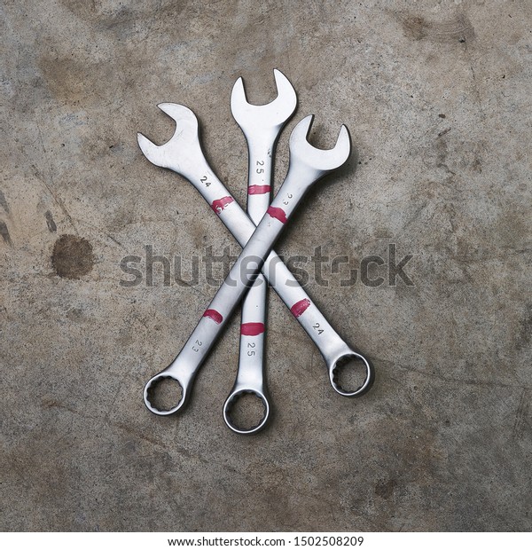 Three crossed wrenches on a concrete floor in a\
car workshop.