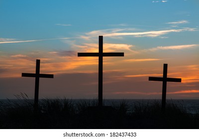 Three crosses with a light clouded sunset behind them.