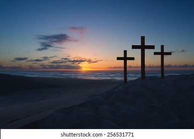 Three crosses on a sand dune next to the ocean with a cloudy sunrise