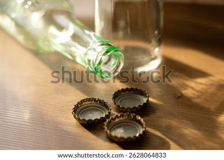 Three crown corks, bottle caps on the table in the kitchen. Empty glass bottles in the background.