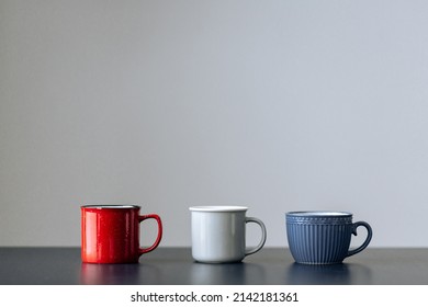 Three cups of different colors on a blue table on a gray background. High quality photo