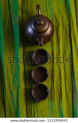 Three cups and a kettle of ceramics on the green background, top view