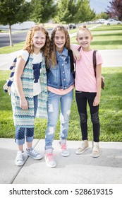 Three cute smiling girls with backpacks on going off to school in the morning