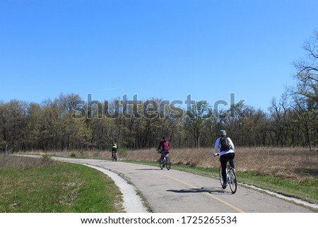 Three cyclists in spring on the North Branch Trail at Miami Woods in Morton Grove, Illinois practicing social distancing