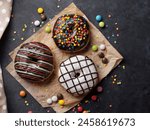 Three Delicious Donuts on Parchment Paper.
This donuts in various colors and flavors, its sprinkled with colorful candies and dusting of confectioners sugar, creating a scene of delightful indulgence.