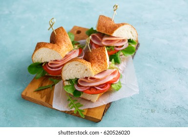 Three delicious ham sandwiches served on a wooden board.
