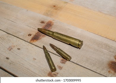 Three difference rifle caliber cartridges laying on barn wood.