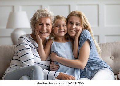 Three different age and generation relatives beautiful females sitting on sofa hugging posing looking at camera. Women or Mother Day holiday celebration, multigenerational family bond and ties concept - Powered by Shutterstock