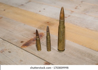Three different caliber rifle bullets standing beside each other against a wooden background.