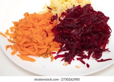 Three different colored vegetables are piled on top of each other on a white plate. The vegetables are carrots, beets, and radishes. The plate is placed on a white table