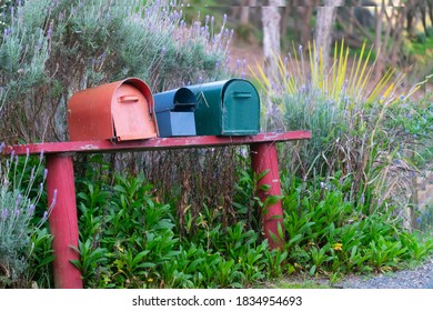 Three different coloured mailboxes together on raodside.
