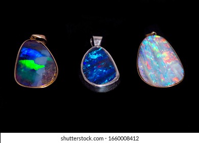 Three Different Colours Of Queensland Boulder Opal Made Into Beautiful And Expensive Pendant Jewelry Set In Gold And Silver Showing Off The Gorgeous Colours And Refraction On A Black Background.