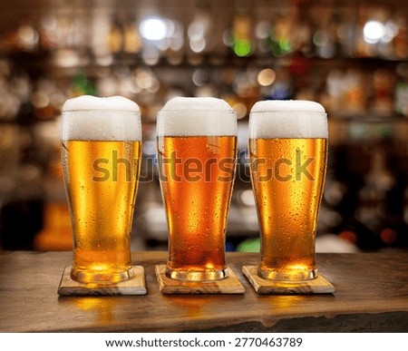 Three different glasses of cold light lager beer with thick white foam and condensation drops on a bar counter background.