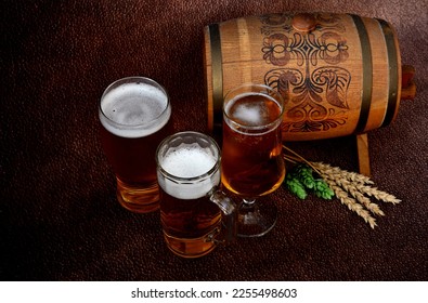Three different glasses with light beer, a wooden keg, ears of barley and ripe hops on a brown background. Close-up.