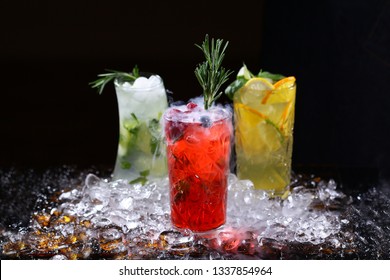 Three different lemonade in high crystal glasses and pieces of ice on the table on a black background. Restaurant or cafe concept