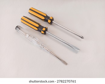 Three different screwdrivers including a Phillips screwdriver, a flathead screwdriver, and a voltage tester pen on a white background.