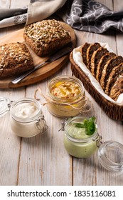 Three different spreading sauces in glass jars with cut whole wheat bread on wooden boards