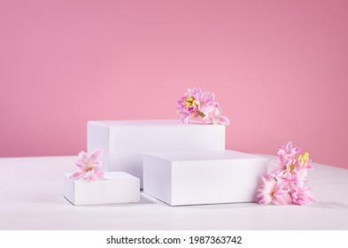 Three Different Square White Podiums For Display Cosmetic Produce Or Goods With Fresh Spring Flowers And Soft Light Pastel Pink Background.