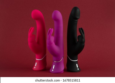 Three dildo in the form of a rabbit stand on a red background. Sex toys for adults. Above view. Place for text. Sex shop concept. Multi-colored vibrators