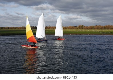 Three dinghy sailing boat on the river Thames at the countryside of Binsey, Oxford, England against a cold overcast cloudy sky.