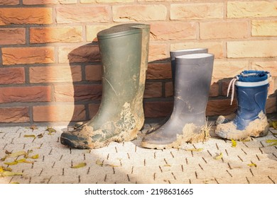 Three Dirty Boots Of All Family Members. Boots Of Child And Parents. In The Fall There Is A Lot Of Work In The Garden. Children Help With Gardening. Lot Of Mud On The Boots.