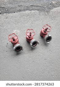 Three dismantled red fire hydrant valves equipped with quick-disconnect fittings are displayed on an asphalt surface during inspection and maintenance.