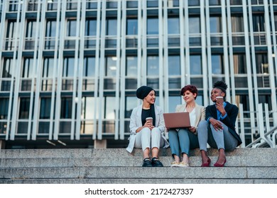 Three Diverse Female Office Workers Are Seated On The Steps In An Urban Setting Of The City's Business District