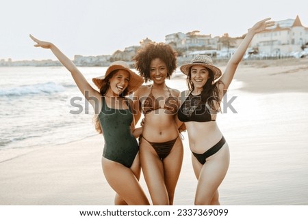 Three diverse girlfriends in swimwear having fun at the beach, women smiling cheerfully while embracing. Happy female friends enjoying their summer vacation