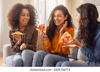 Three diverse women friends enjoying snacks and joyful chat, laughing together while eating pizza on a cozy sofa in modern living room interior. Home gathering, female friendship - Powered by Shutterstock