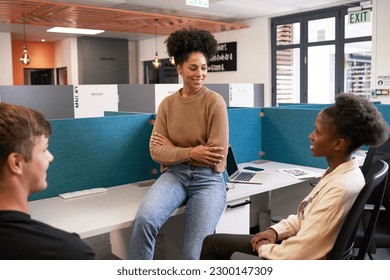 Three diverse young colleagues have an informal meeting, bright open plan office