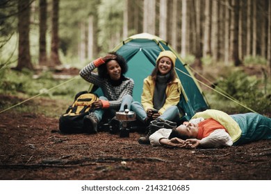 Three diverse young female friends laughing together while relaxing at their campsite in a forest - Powered by Shutterstock