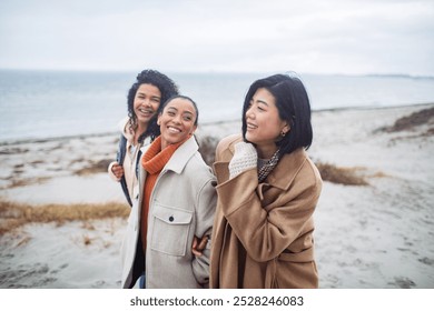 Three diverse young female friends walking on the beach in winter - Powered by Shutterstock