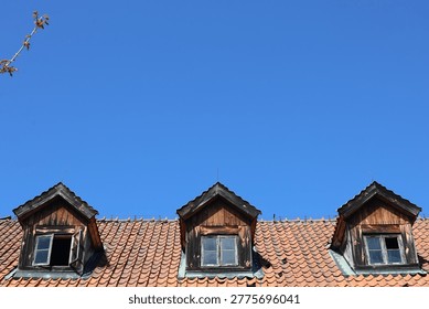 Three Dormer Windows on an Old Tiled Roof Against a Blue Sky