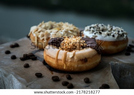 Three doughnuts covered with Choco peanut butter, Cookies and creme and Almendras on wooden cutting board. The concept of delicious glazed donuts, Space for text, Selective Focus.