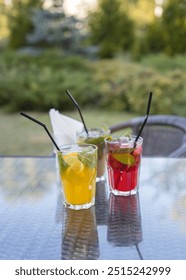 Three drinks on a table with straws in them. One is orange, one is red, and one is green