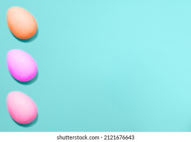 Three Easter eggs colored with violet, pink and coral colors from left side on a blue background. Flat lay. Copy space for text, mock up. Banner.