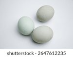 Three eggs are sitting on a white surface. The eggs are all different sizes and colors. The eggs are arranged in a row, with the largest egg on the left and the smallest egg on the right