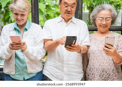 Three elderly people using smartphones, smiling and engaged. Diverse group enjoying technology, standing together, sharing moments with phones. Diverse senior people using social media. - Powered by Shutterstock