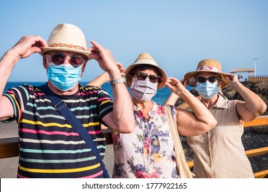 Three Elderly People Wearing Medical Mask Because Of Coronavirus Hold Their Hat While Enjoying Freedom And Beach Holidays - Active Retired Senior Adult