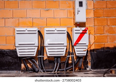 Three electrical distribution boxes installed on orange brick wall with visible black cables, one box marked with red diagonal stripe. Outdoor cabinets for low voltage power and electricity supply.