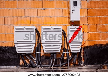 Three electrical distribution boxes installed on orange brick wall with visible black cables, one box marked with red diagonal stripe. Outdoor cabinets for low voltage power and electricity supply.
